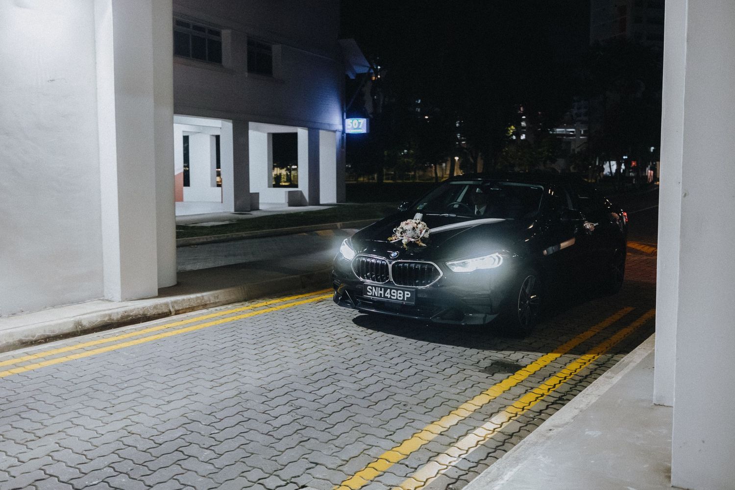 Car headlights illuminate a dimly lit parking garage entrance with yellow safety markings on concrete floor.