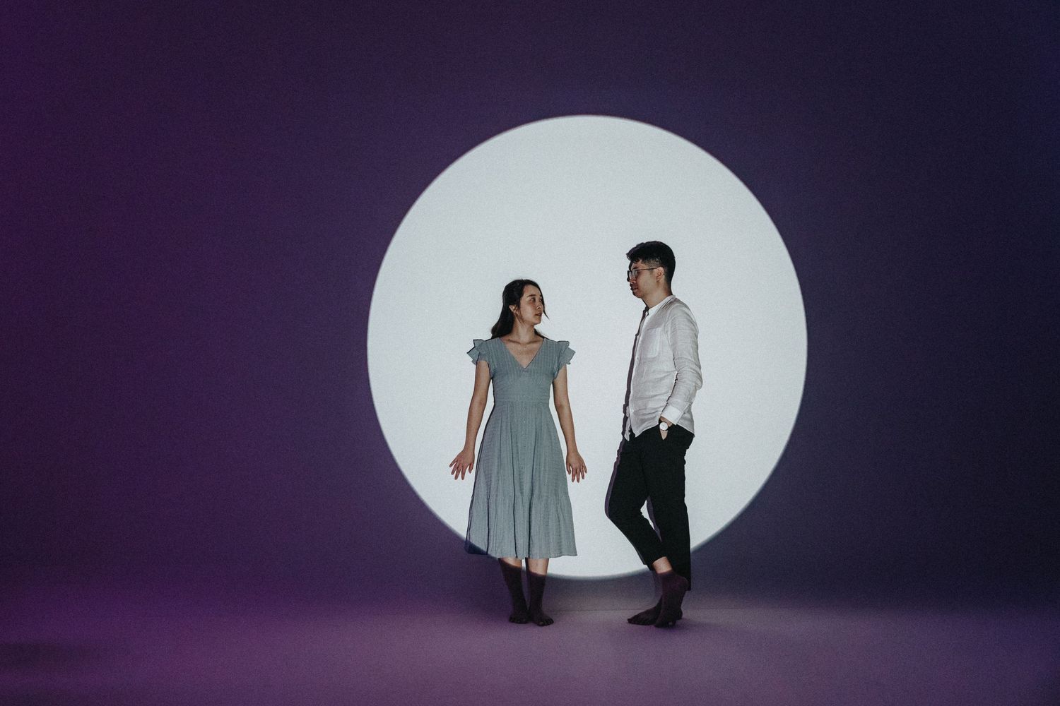 Artistic silhouette portraits of two people against a dramatic purple backdrop with spotlight.