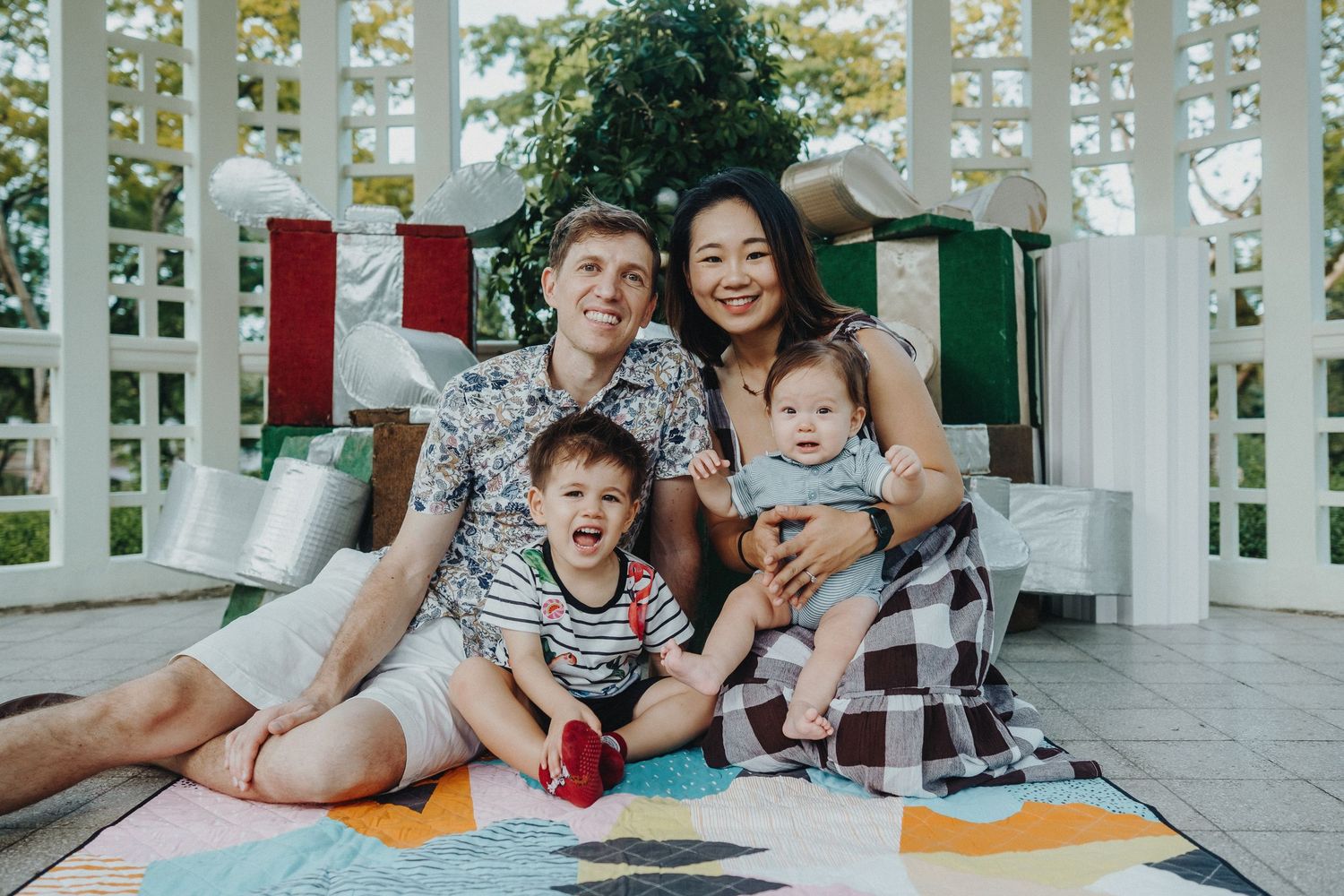 A family group sits together on a porch with holiday decorations, smiling and sharing a joyful moment while looking at books.