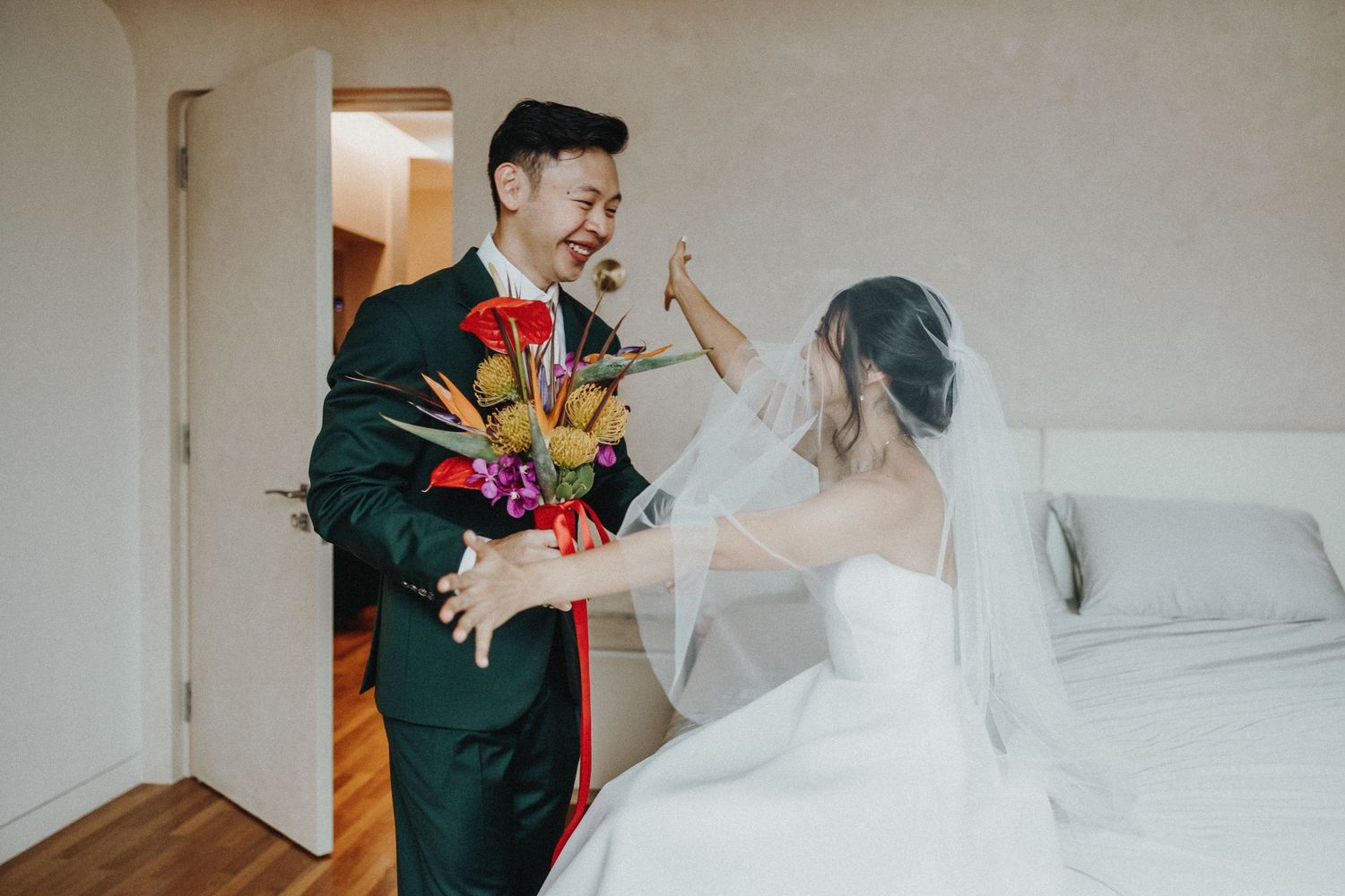 A couple shares a playful moment in their wedding attire with a bright bouquet of tropical flowers.