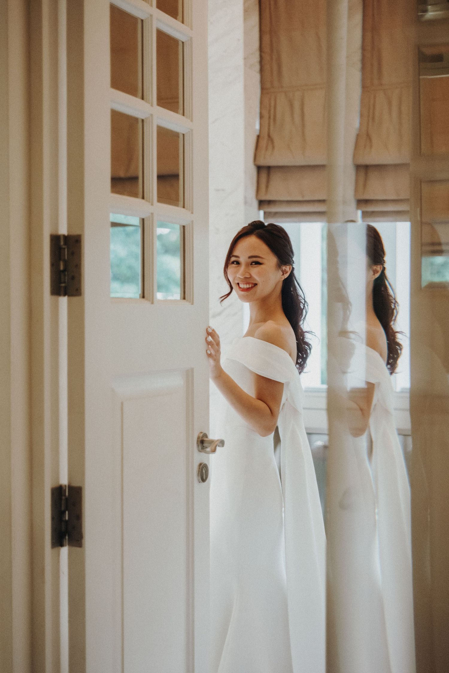 A bride in a classic white wedding dress stands between mirrored closet doors creating a reflective effect.