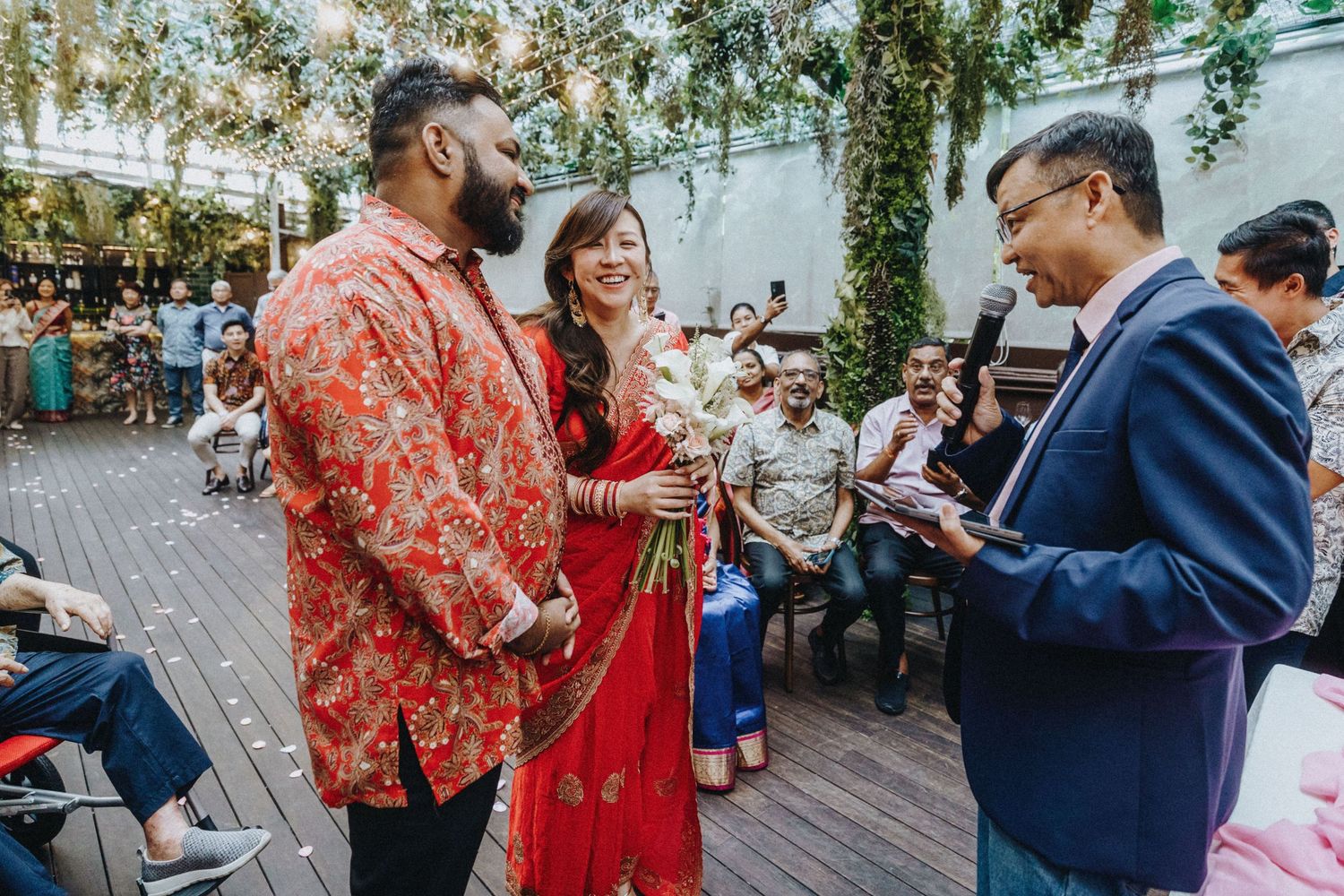 A couple in traditional Indian attire exchange vows outdoors at a garden wedding ceremony.