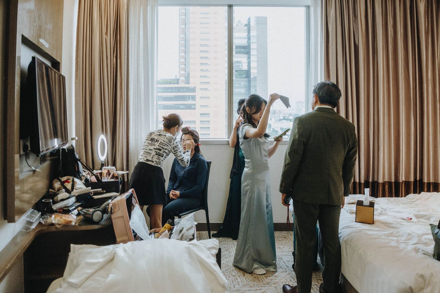Bridal party getting ready in a hotel room, with makeup and hair styling before a wedding ceremony.
