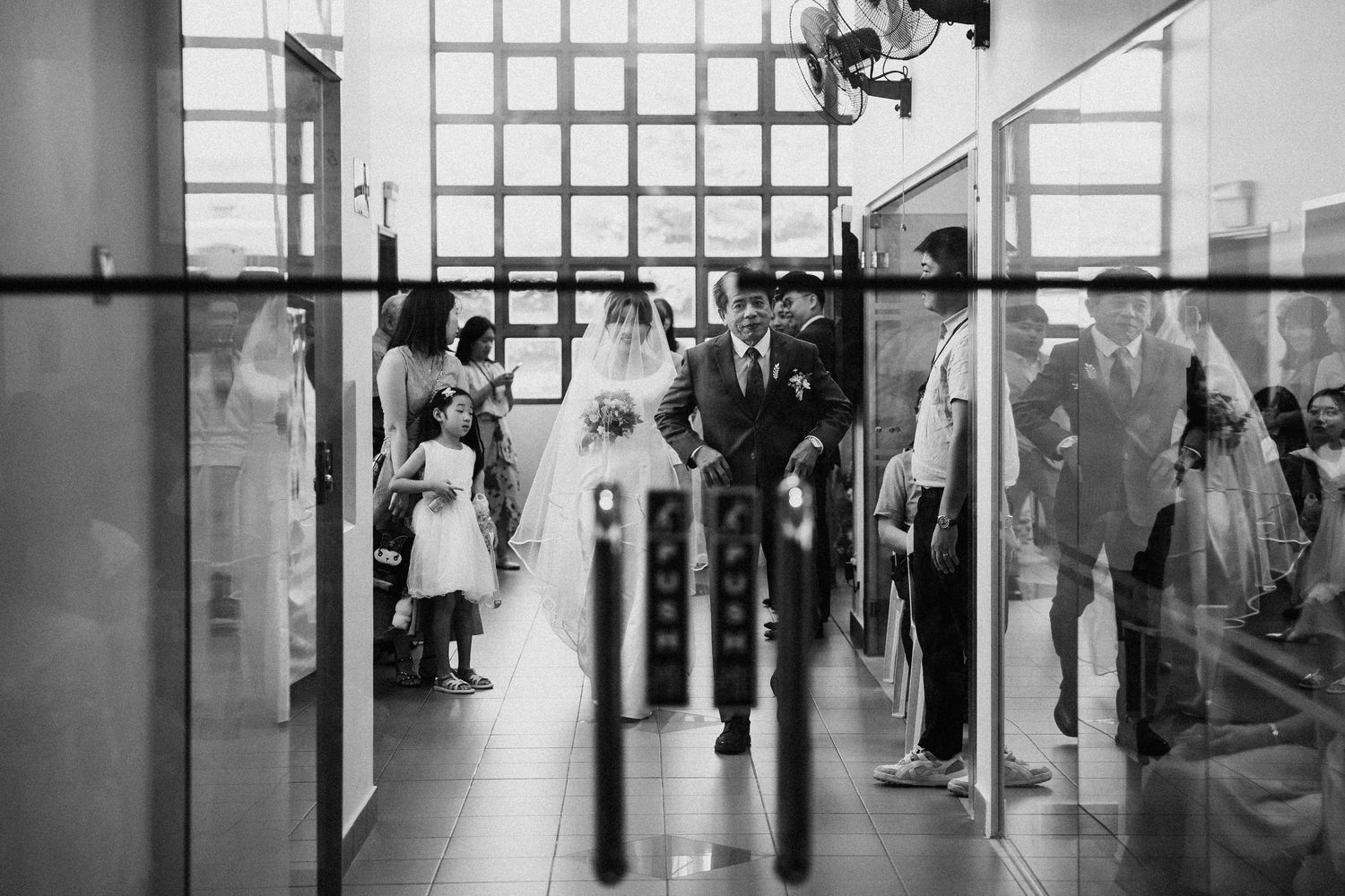 Black and white photo of a bride walking down the aisle with her father during a wedding ceremony.
