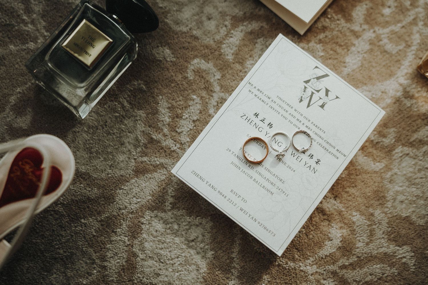 Wedding rings and invitation displayed with perfume bottle on textured surface.