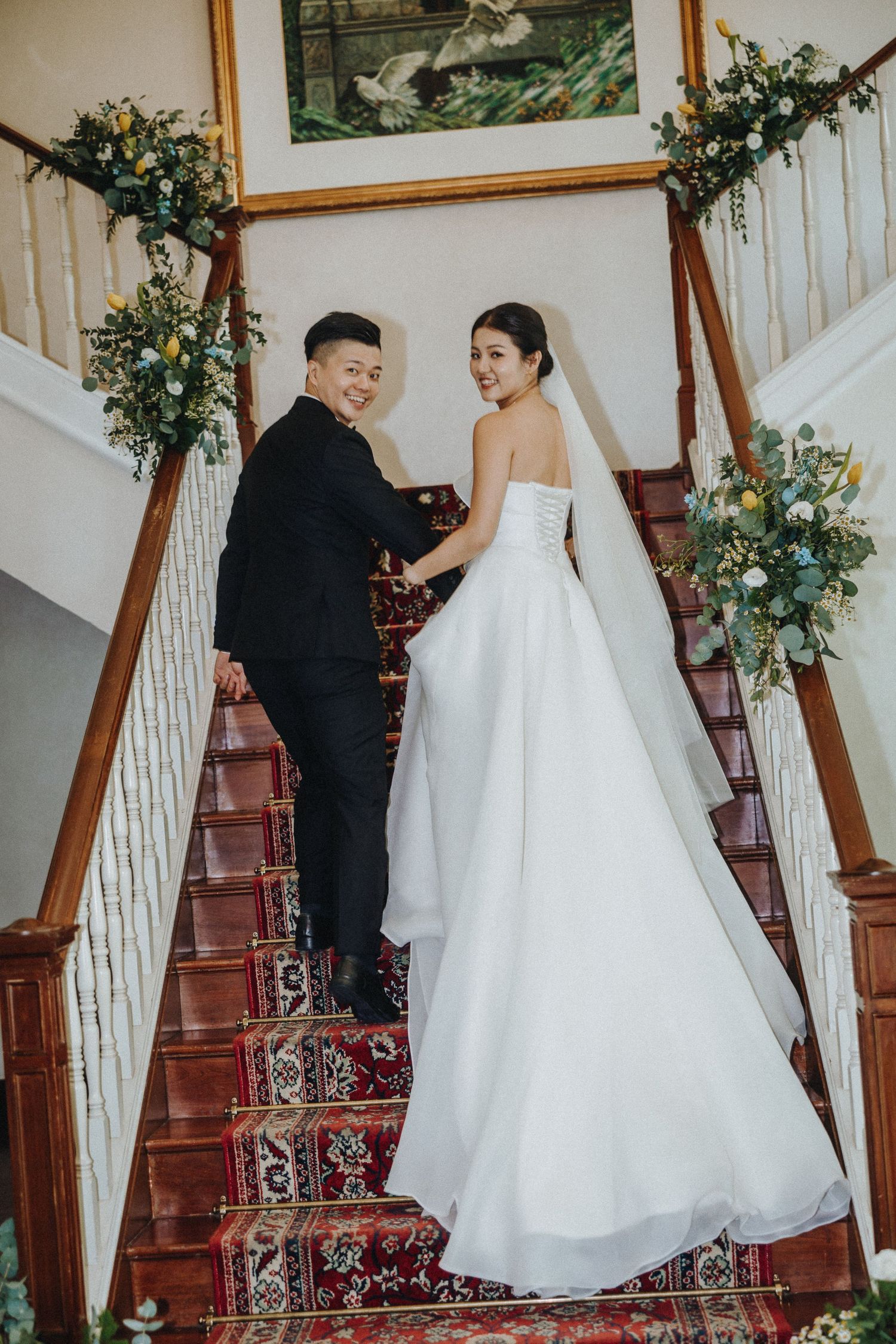 Wedding couple interacts on an elegant staircase decorated with floral garlands.