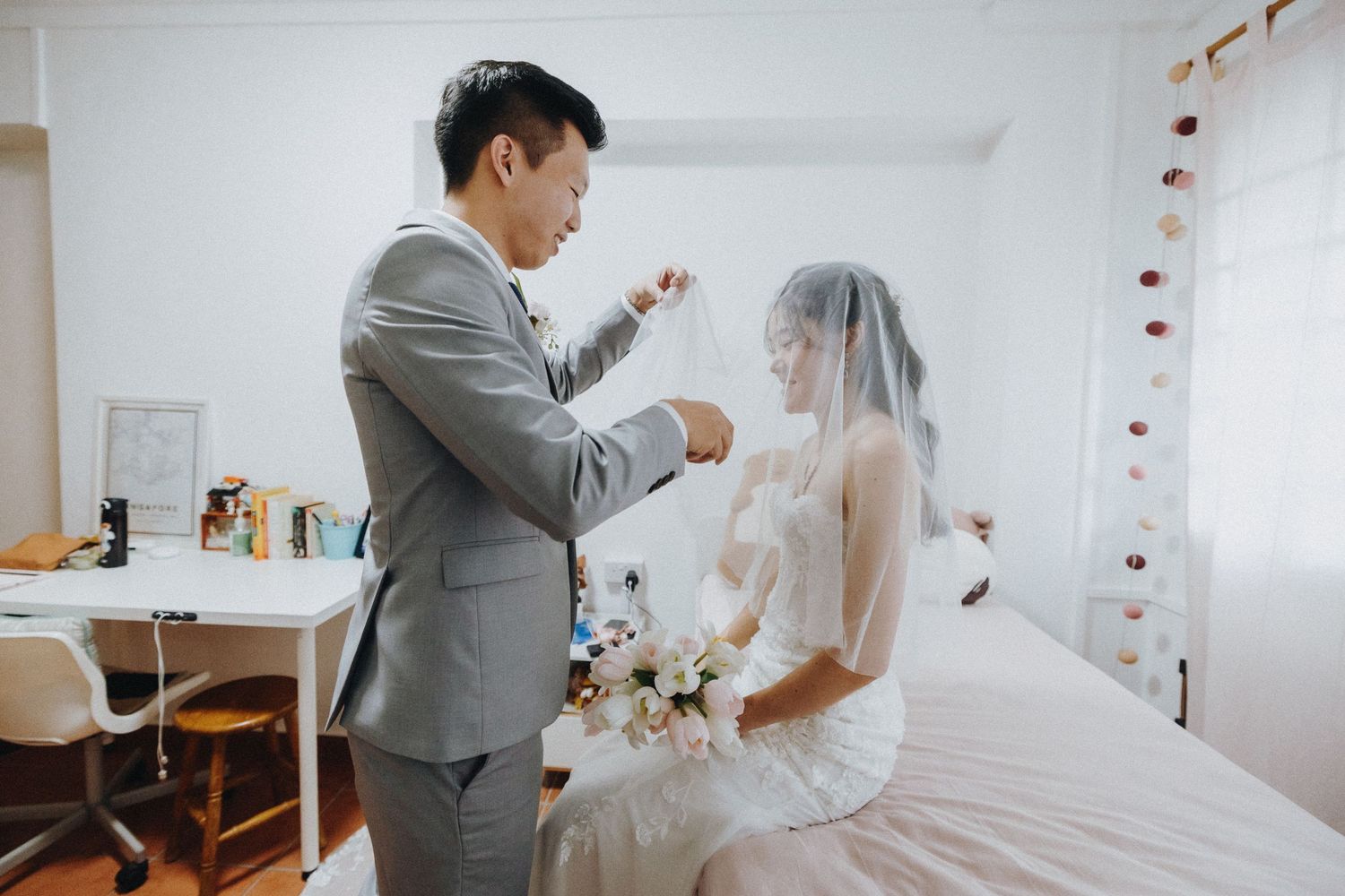 Wedding couple shares intimate first look moment in bright white room with string lights.