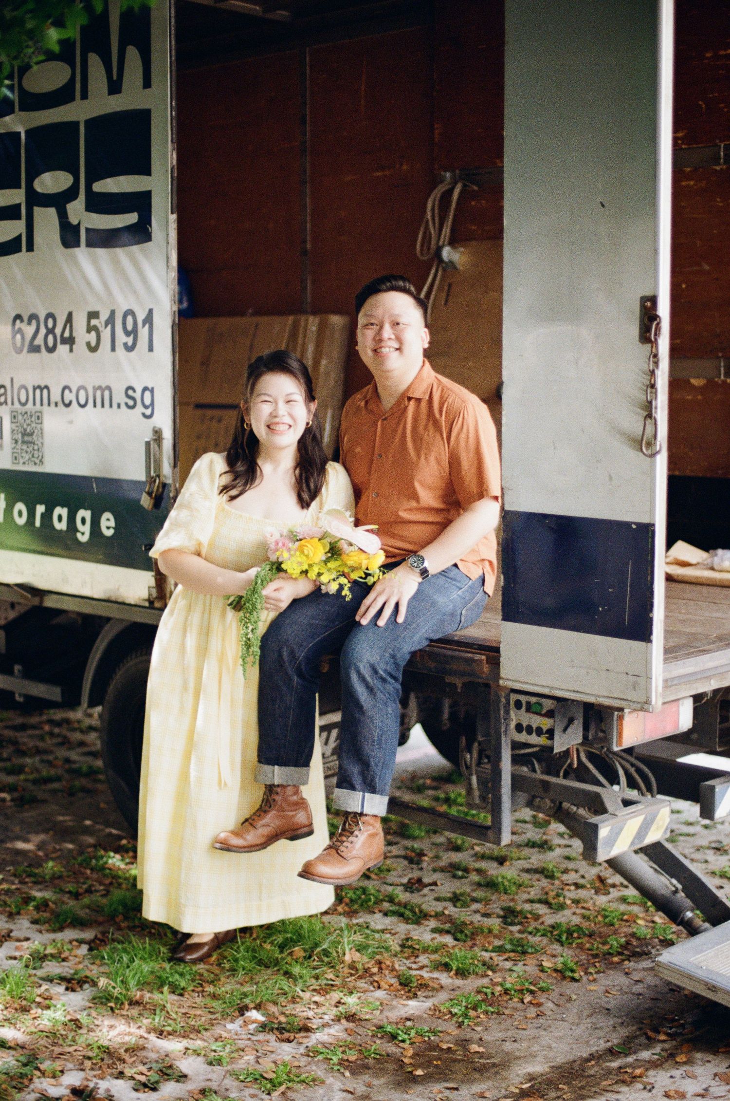 A couple sits together on a delivery truck with bright smiles and casual attire.