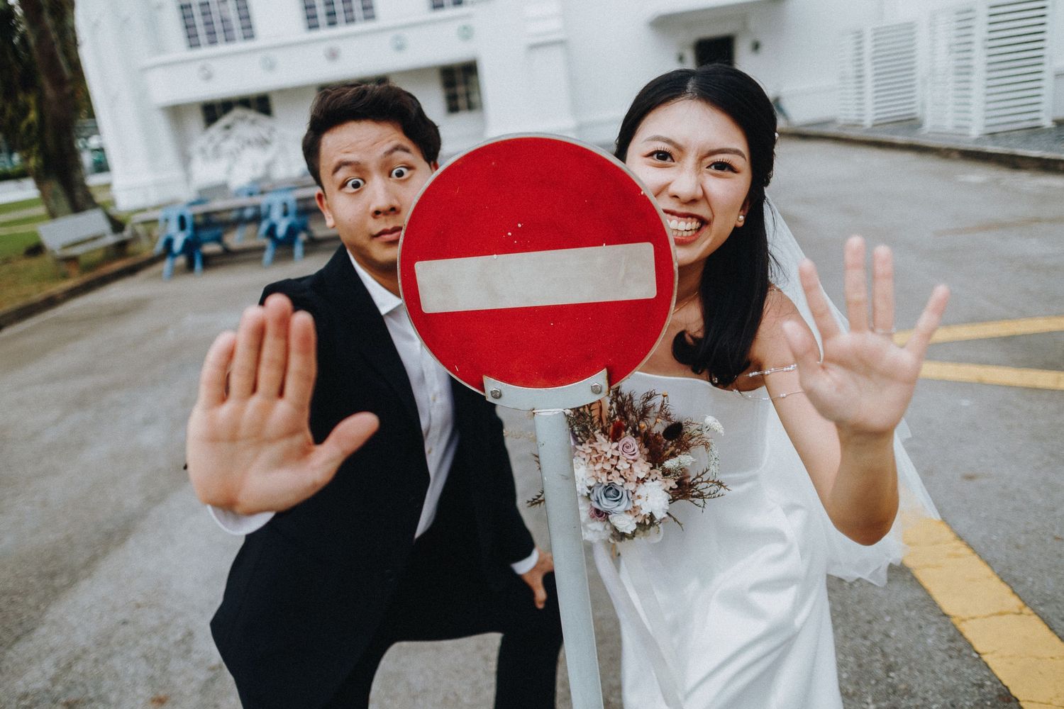 A couple poses playfully with a red no-entry traffic sign in a fun wedding photo.