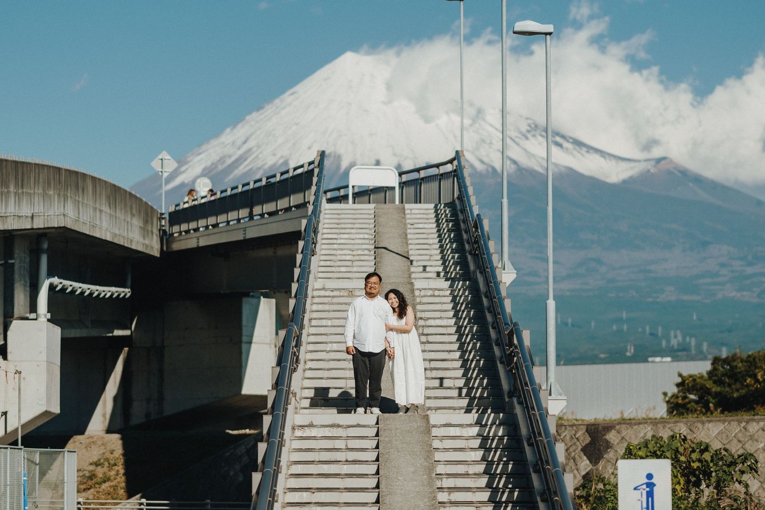 Modern black metal stairway with handrails leads up the side of an industrial building against a blue mountain backdrop.