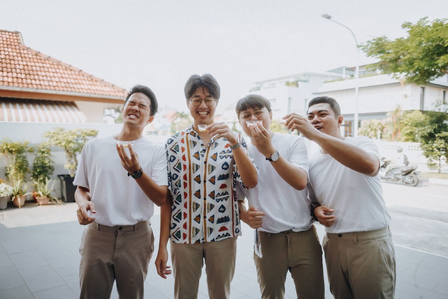 Four people laughing together outdoors on a sunny day wearing casual clothes and standing in front of a house.