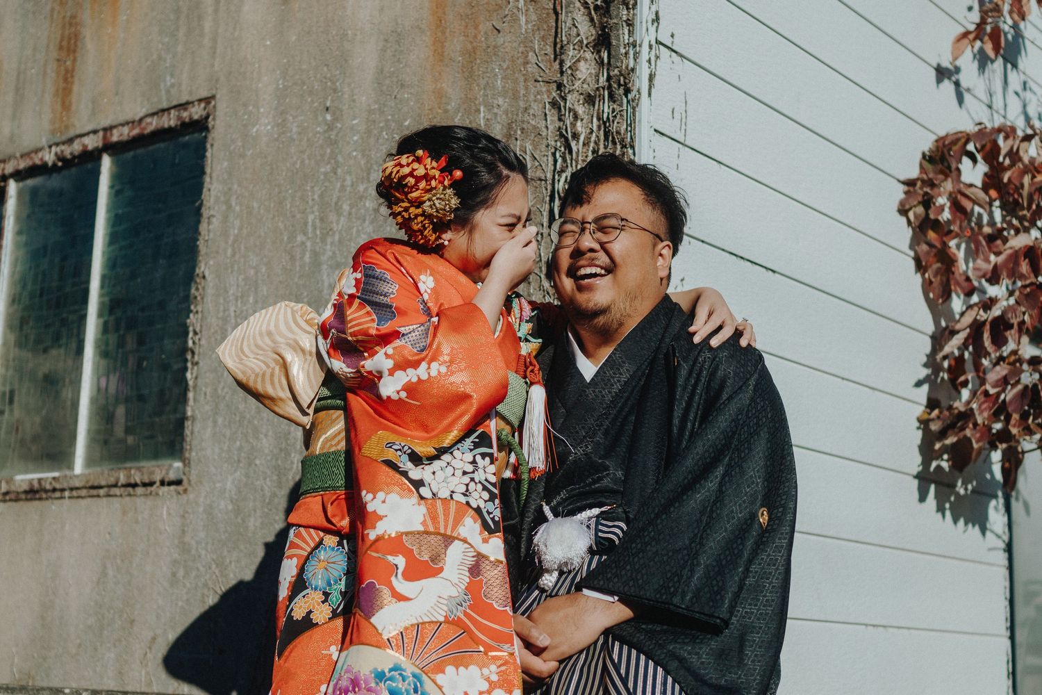 Couple in traditional Japanese attire sharing joyful moment against weathered wall.