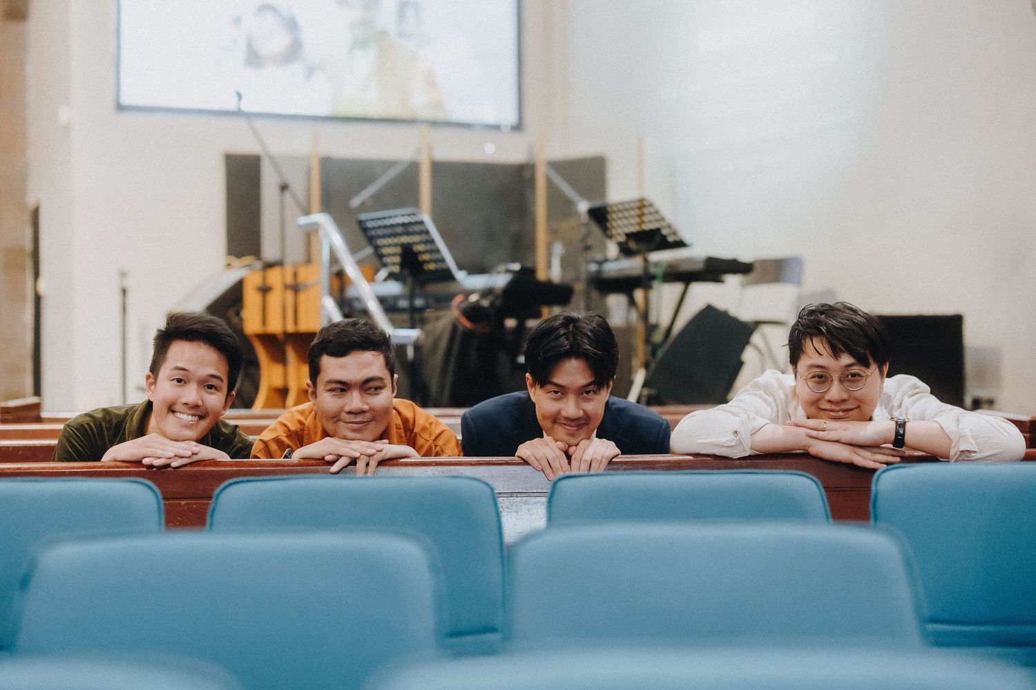 People peek playfully over blue chairs in what appears to be a church or auditorium setting.