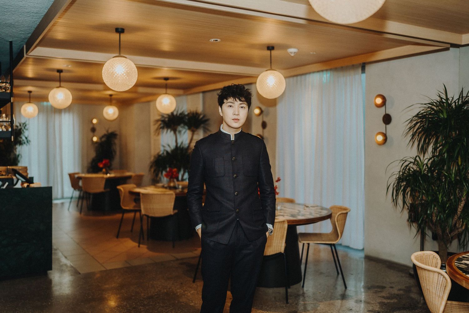A stylish restaurant interior featuring pendant lights and modern decor with a staff member in black attire.