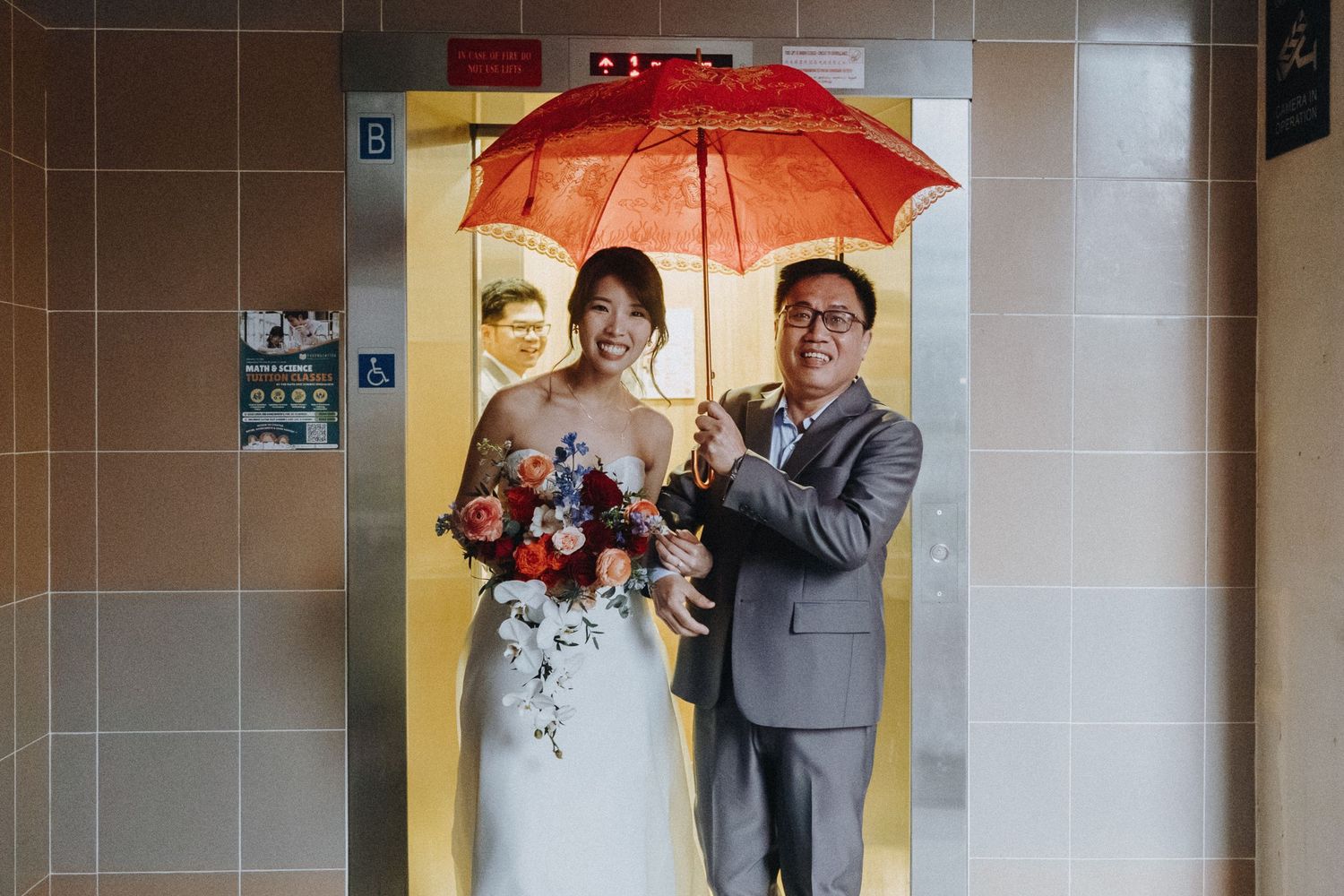 Wedding party poses with a red umbrella against a brick and tile wall at an indoor venue.