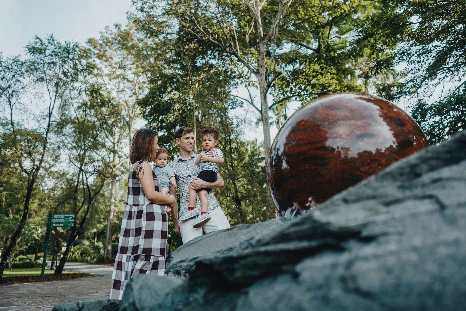 Family stands together in park with large spherical sculpture visible in foreground.