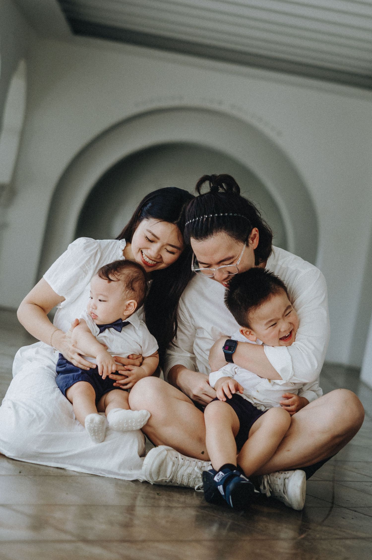 A family in matching white outfits shares a joyful moment while sitting under an archway.