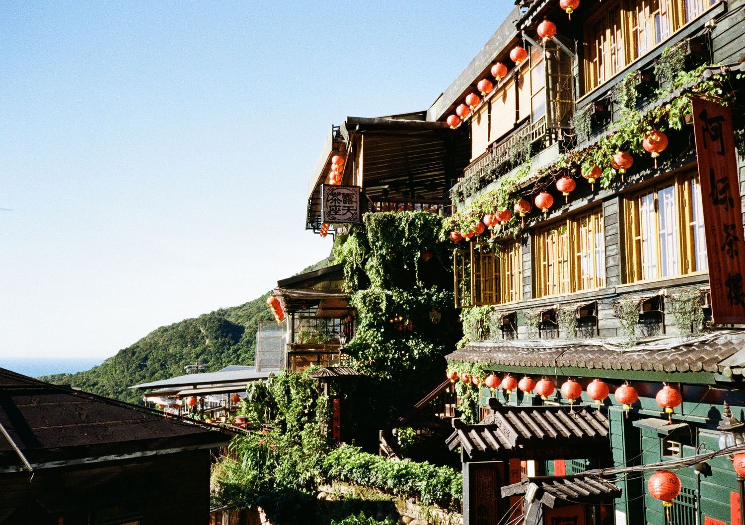 Traditional wooden teahouse with ornate balconies and floral decorations on a hillside in Asia.