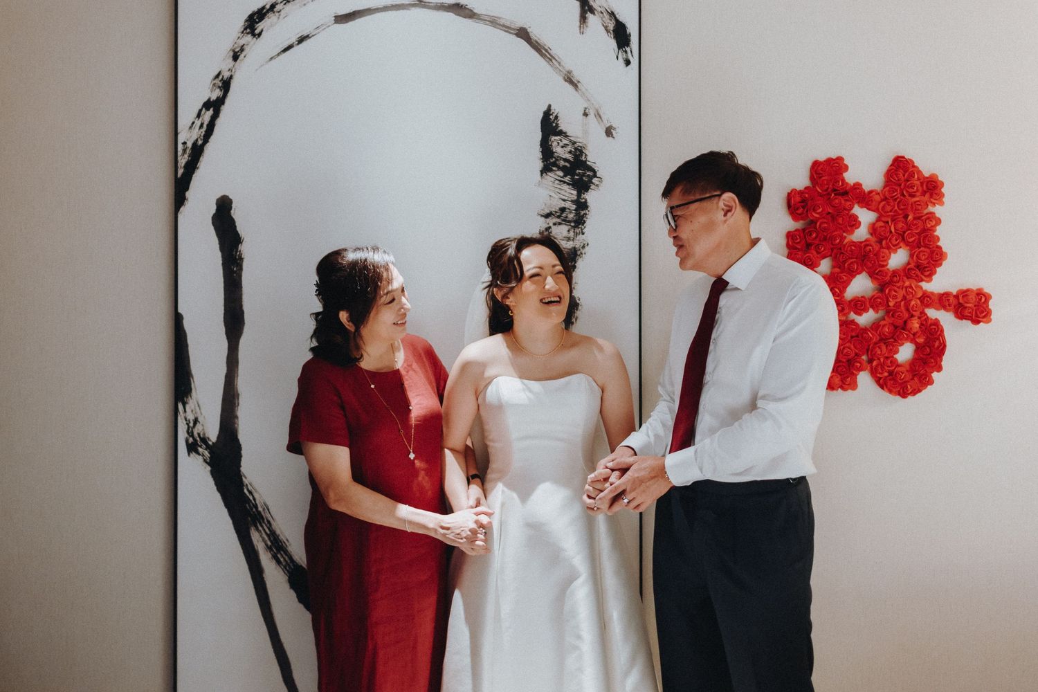 Wedding party poses against white wall with red floral decorations during intimate ceremony.