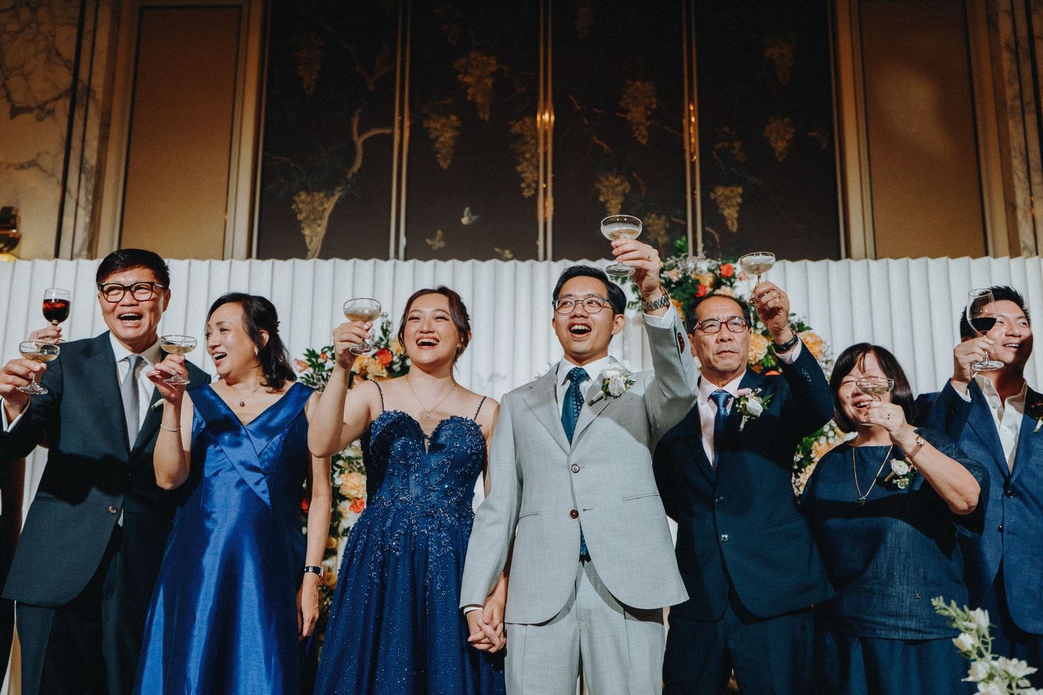 Wedding party members react with excitement and joy during a celebration in formal attire.