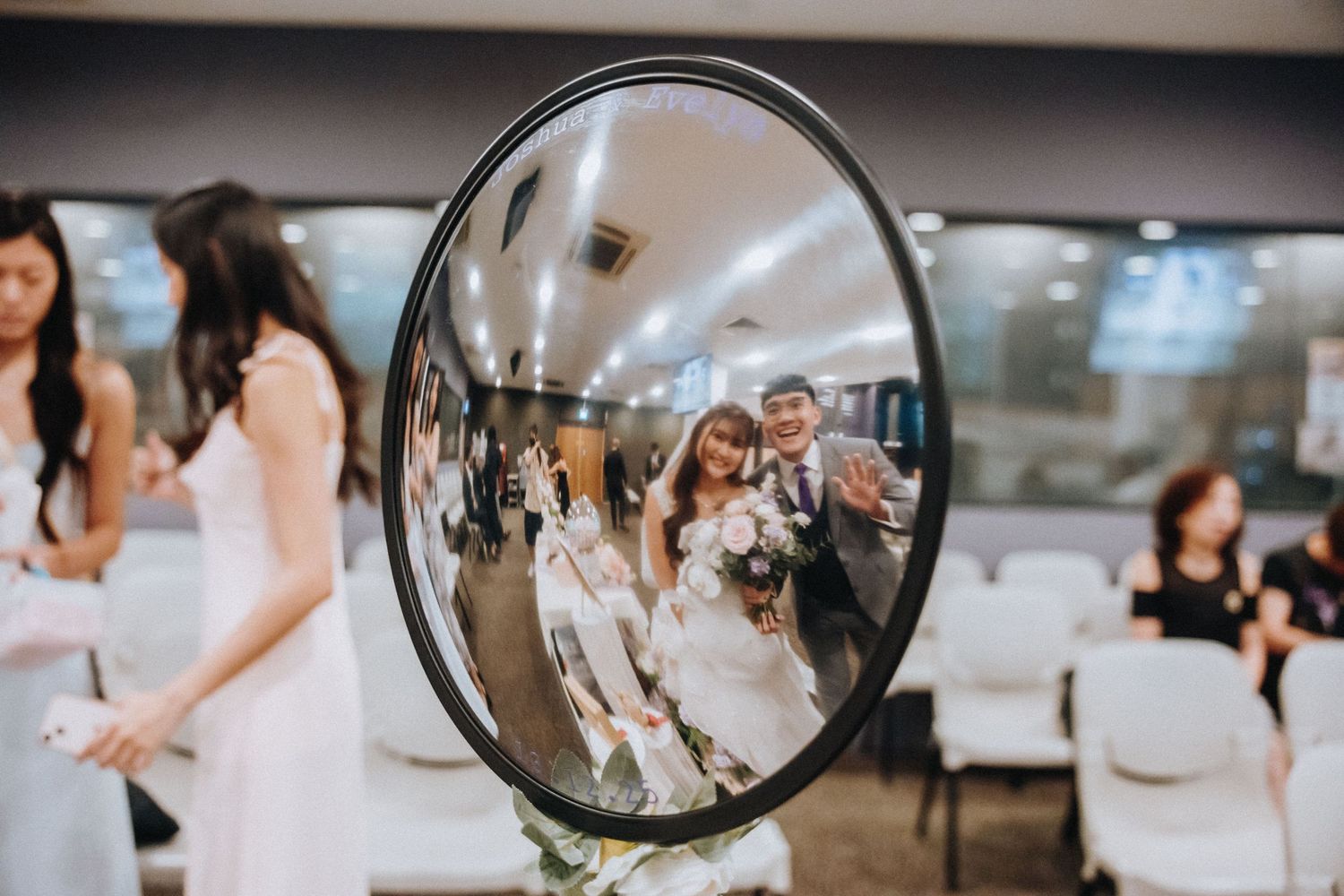 A convex mirror reflects a wedding celebration scene with guests gathered in a reception space.