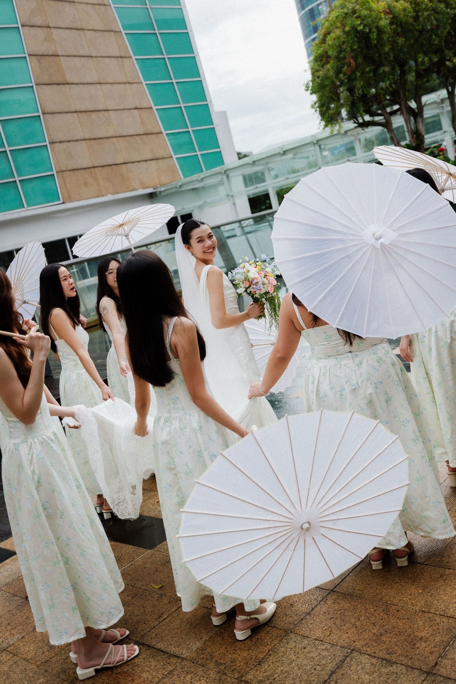 Bride holding bouquet with bridesmaids in white dresses holding paper parasols outdoors at a wedding.