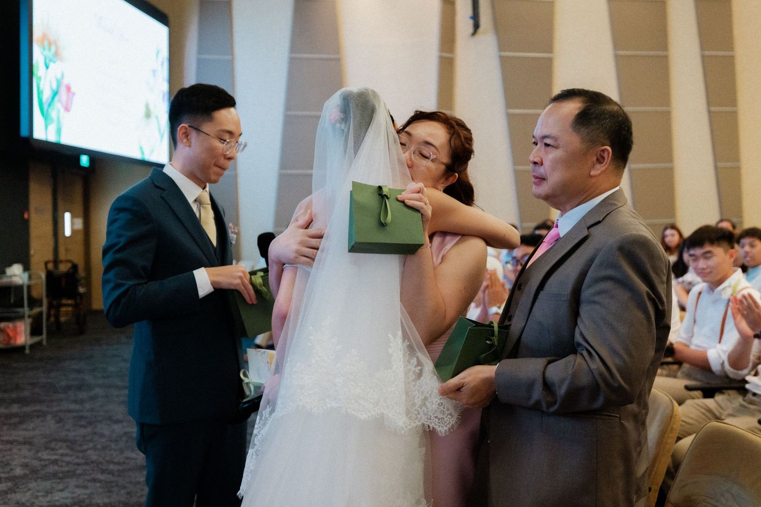 Bride receives veil from family members during emotional wedding ceremony indoors.