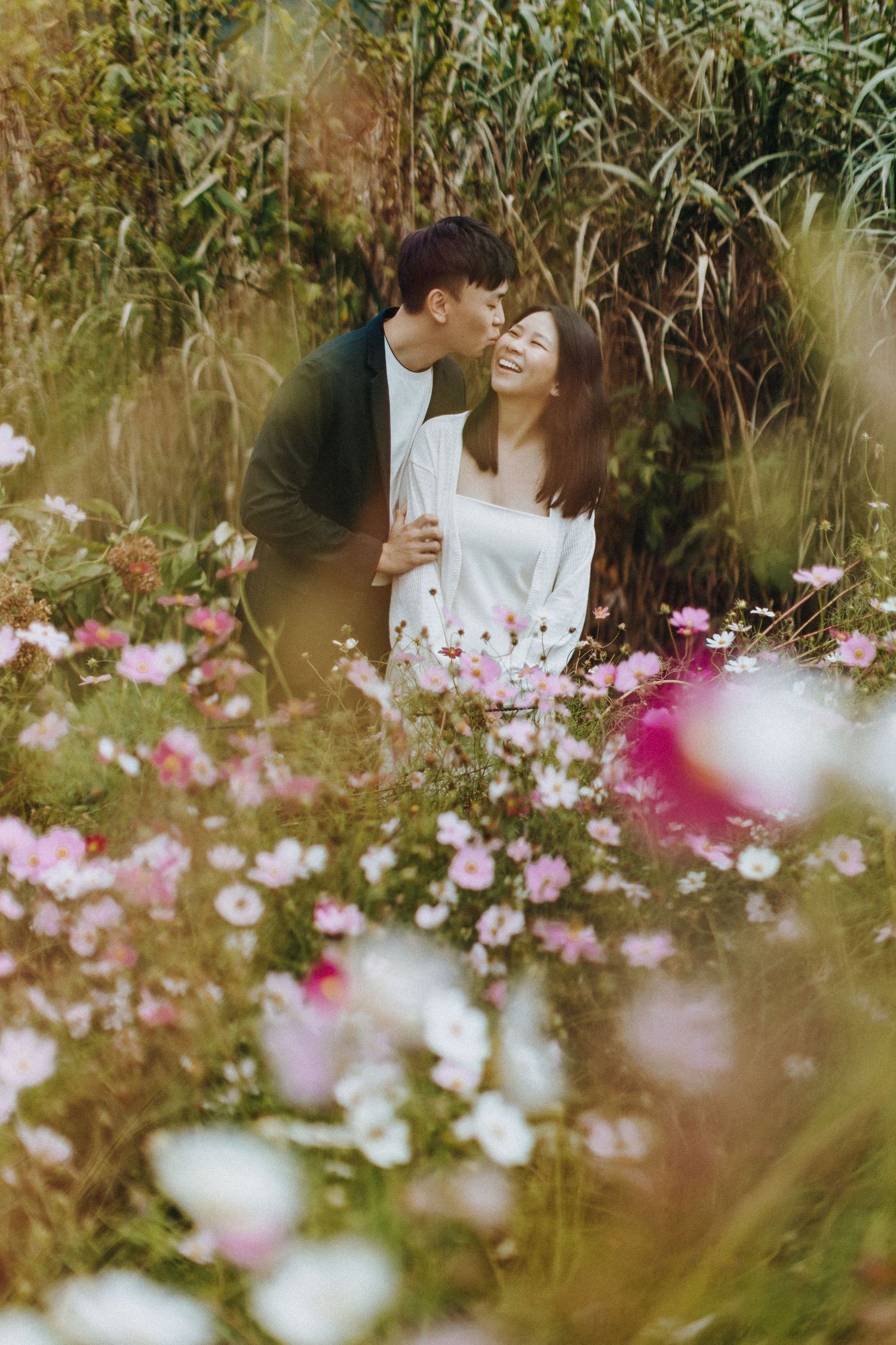 Romantic couple surrounded by blooming pink cosmos flowers in a garden setting.