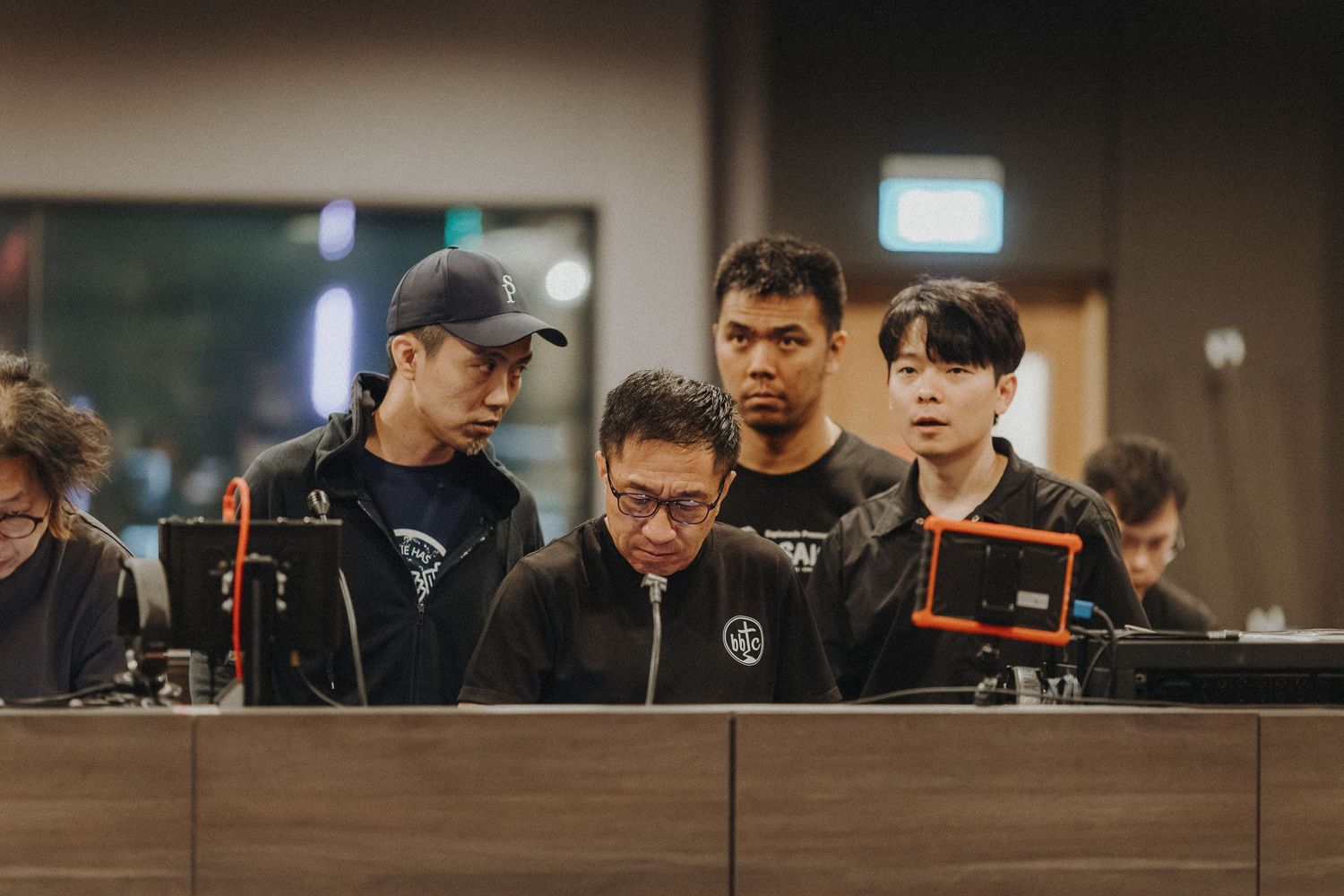 Esports team members huddle together at gaming tournament viewing monitors in dark room during competition.