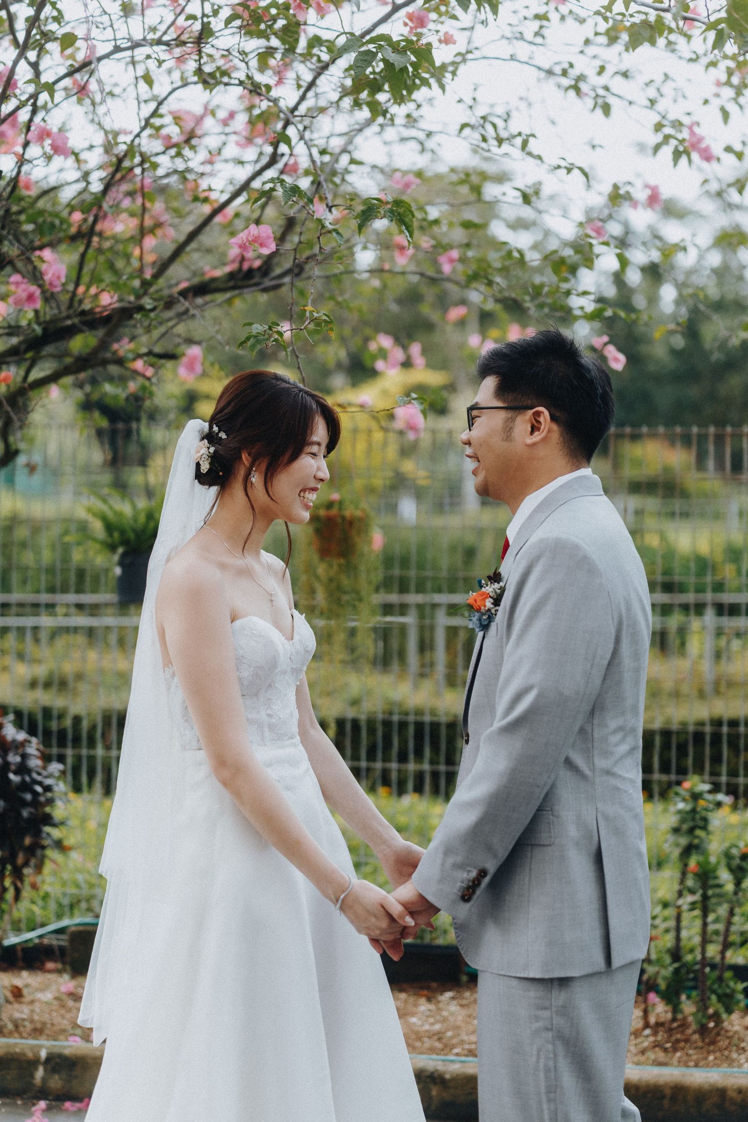 Romantic wedding portrait under blooming cherry blossoms in a garden setting.