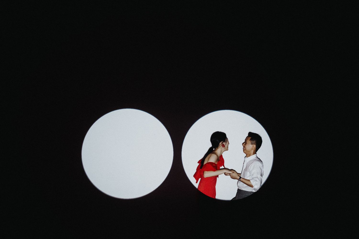 Two people looking at phones through a circular opening against a dark background.