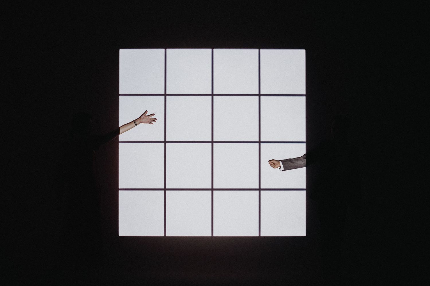 Two hands reach inward from opposite sides against a white geometric grid background creating minimal contrast.