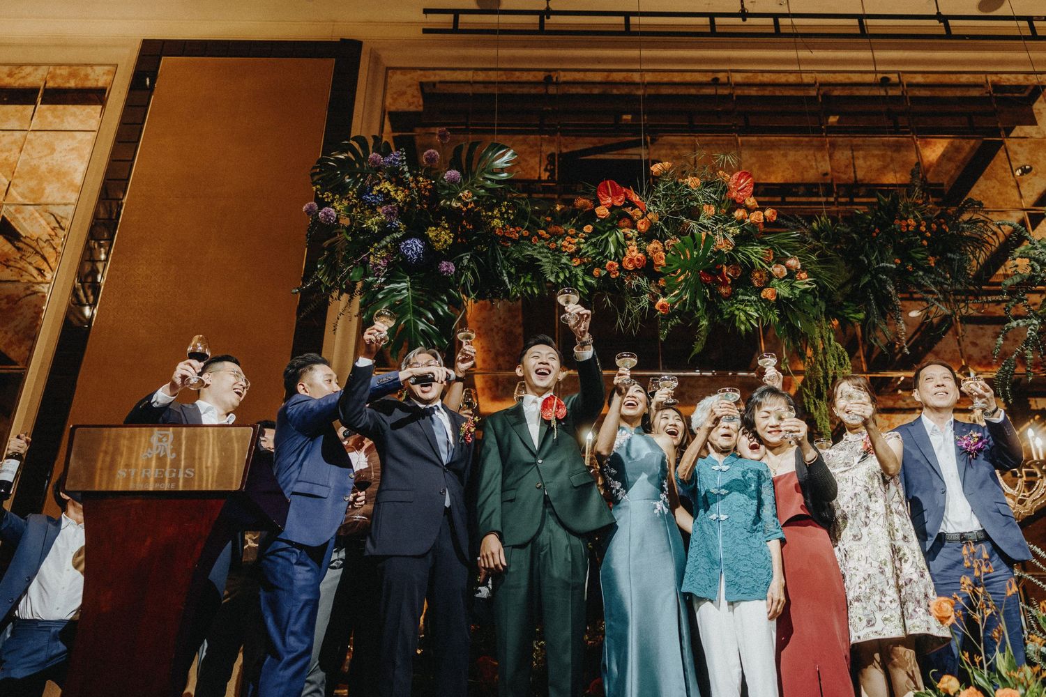 Wedding guests line up against a rustic brick wall to celebrate the newlyweds.