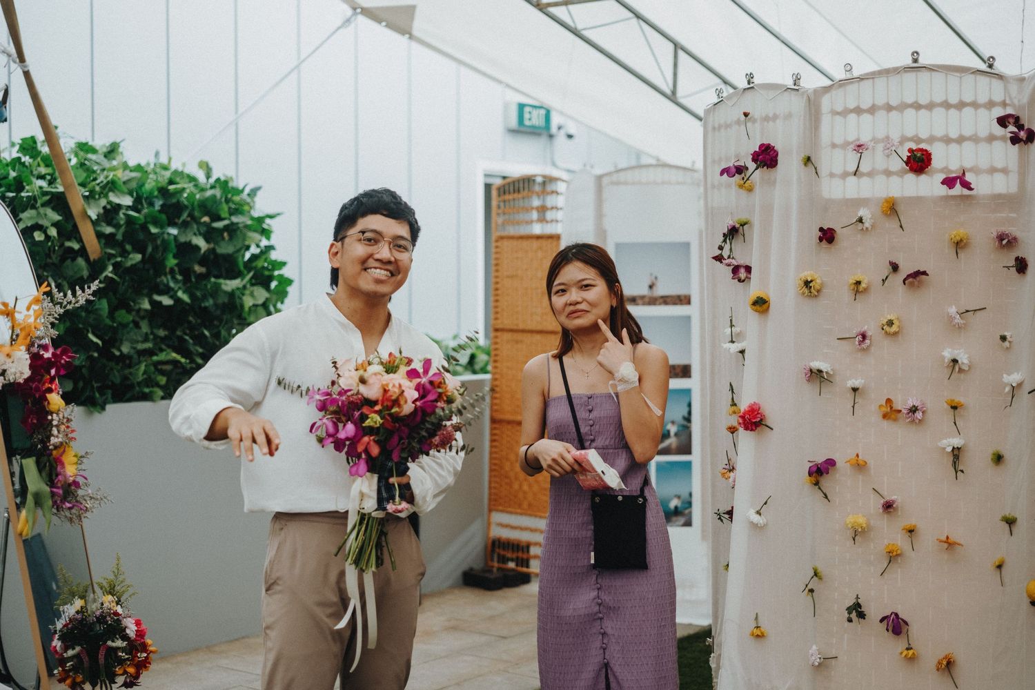 Two people arrange vibrant flowers in a greenhouse with a decorative wall display.