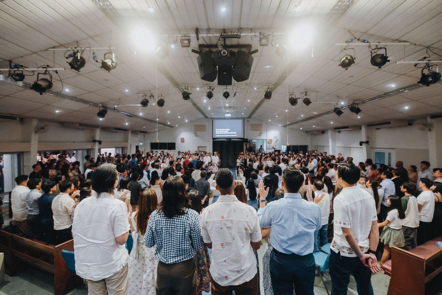 A large crowd of people gathered in a white-ceiling venue with stage lighting equipment.