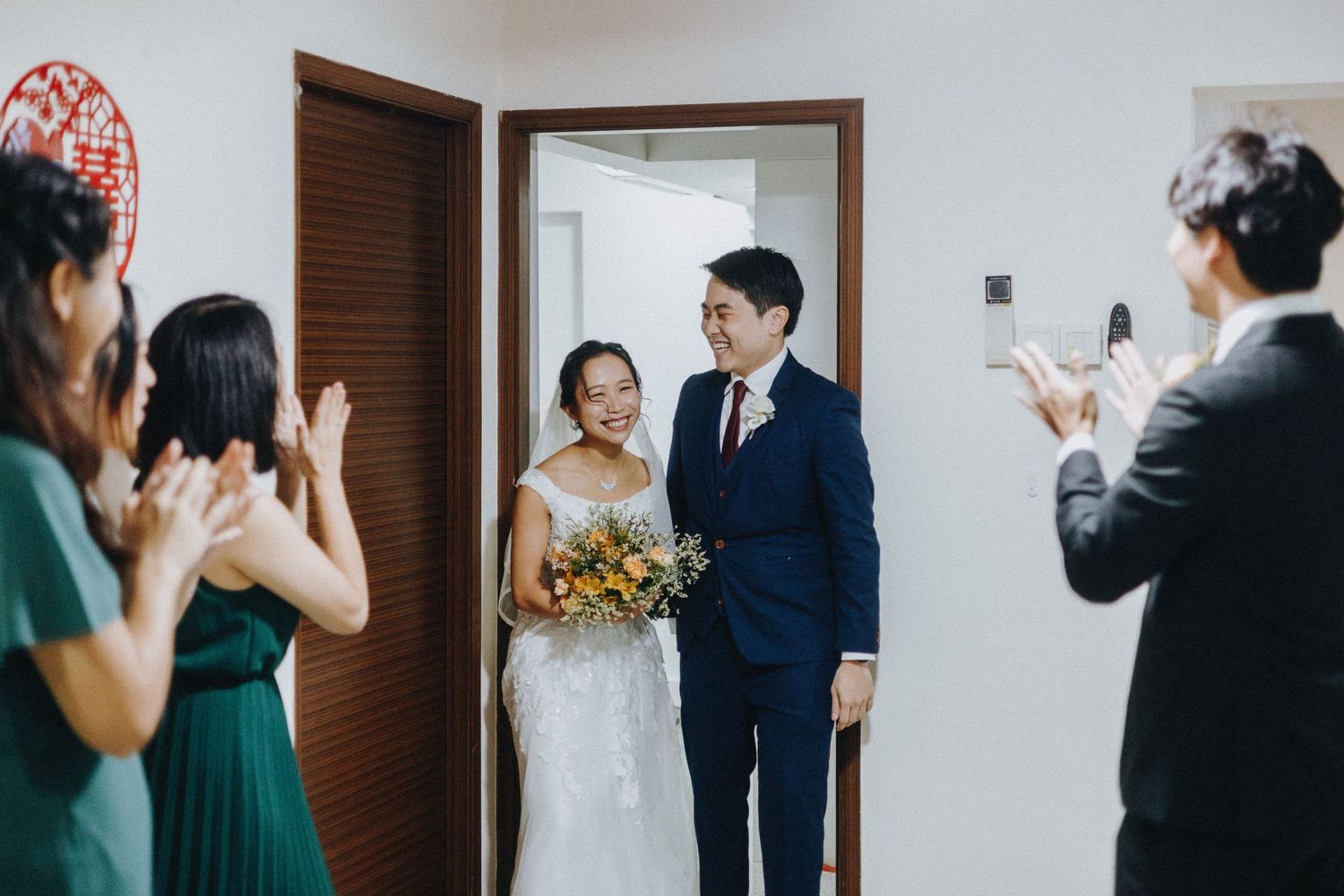 Wedding guests wave goodbye at a heartwarming reception celebration with a rustic wooden door backdrop.