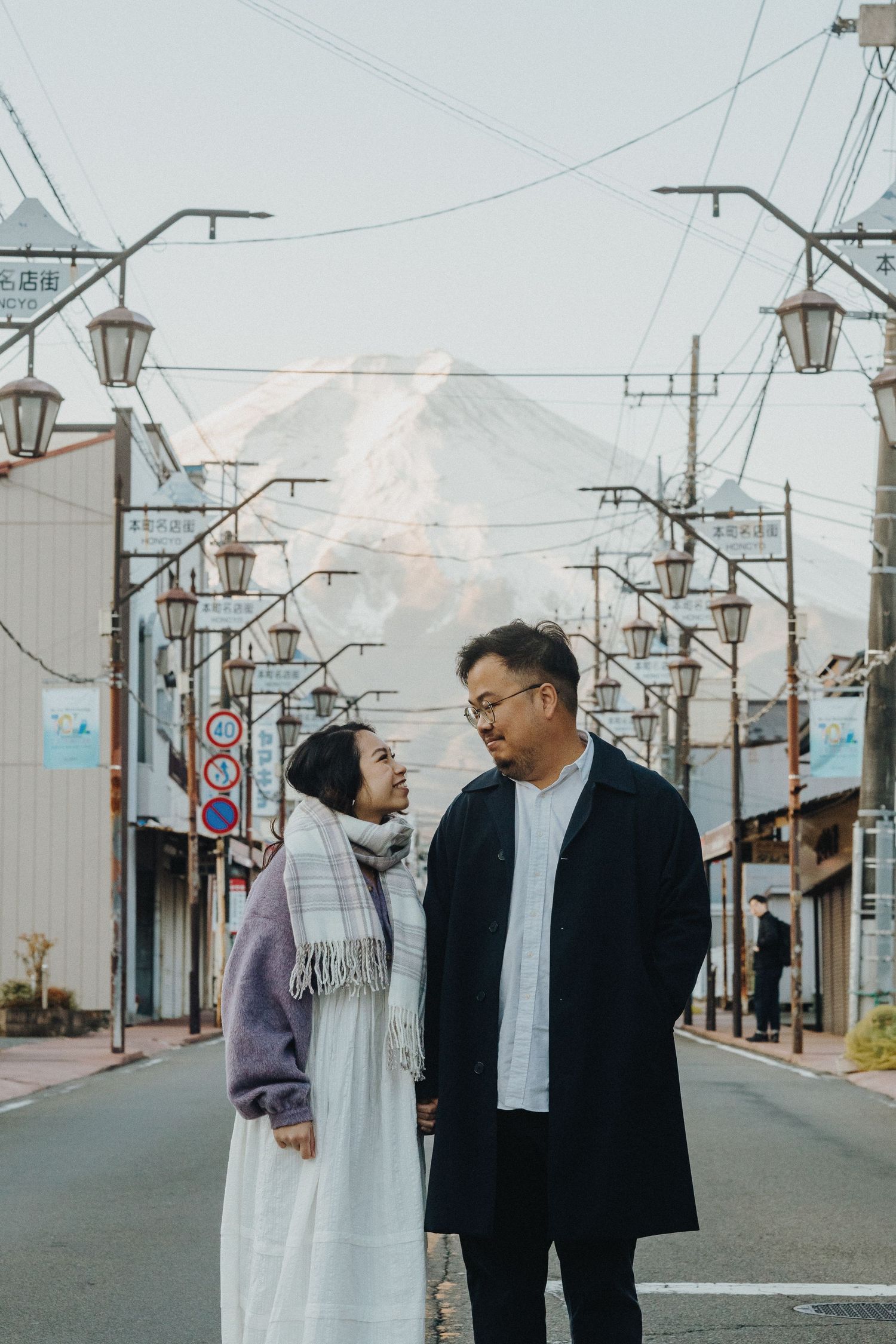 Two people having a conversation on a street with power lines and street lamps.