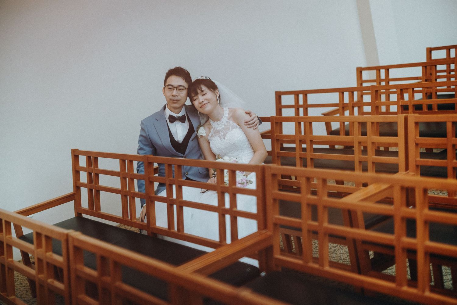 A happy pair sit together among wooden church pews in a bright interior setting.