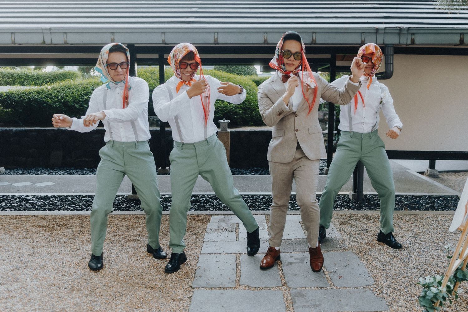 Four people in matching sage green pants and white tops pose playfully in a coordinated group photo.