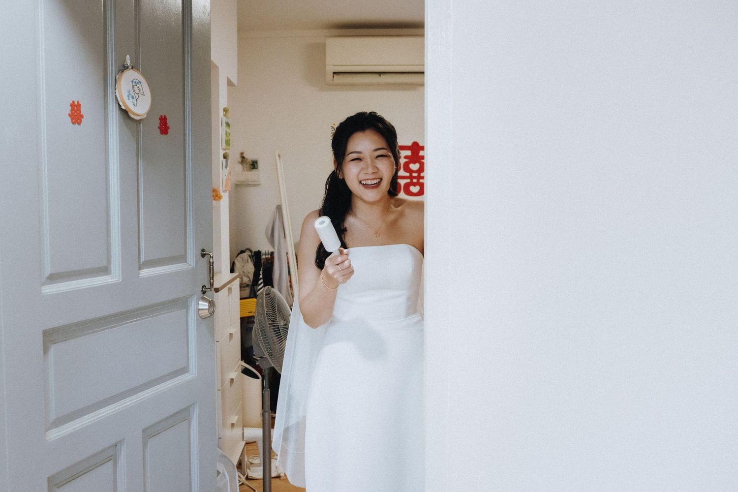 Radiant bride in white strapless gown smiles while holding bouquet near decorated doorway.
