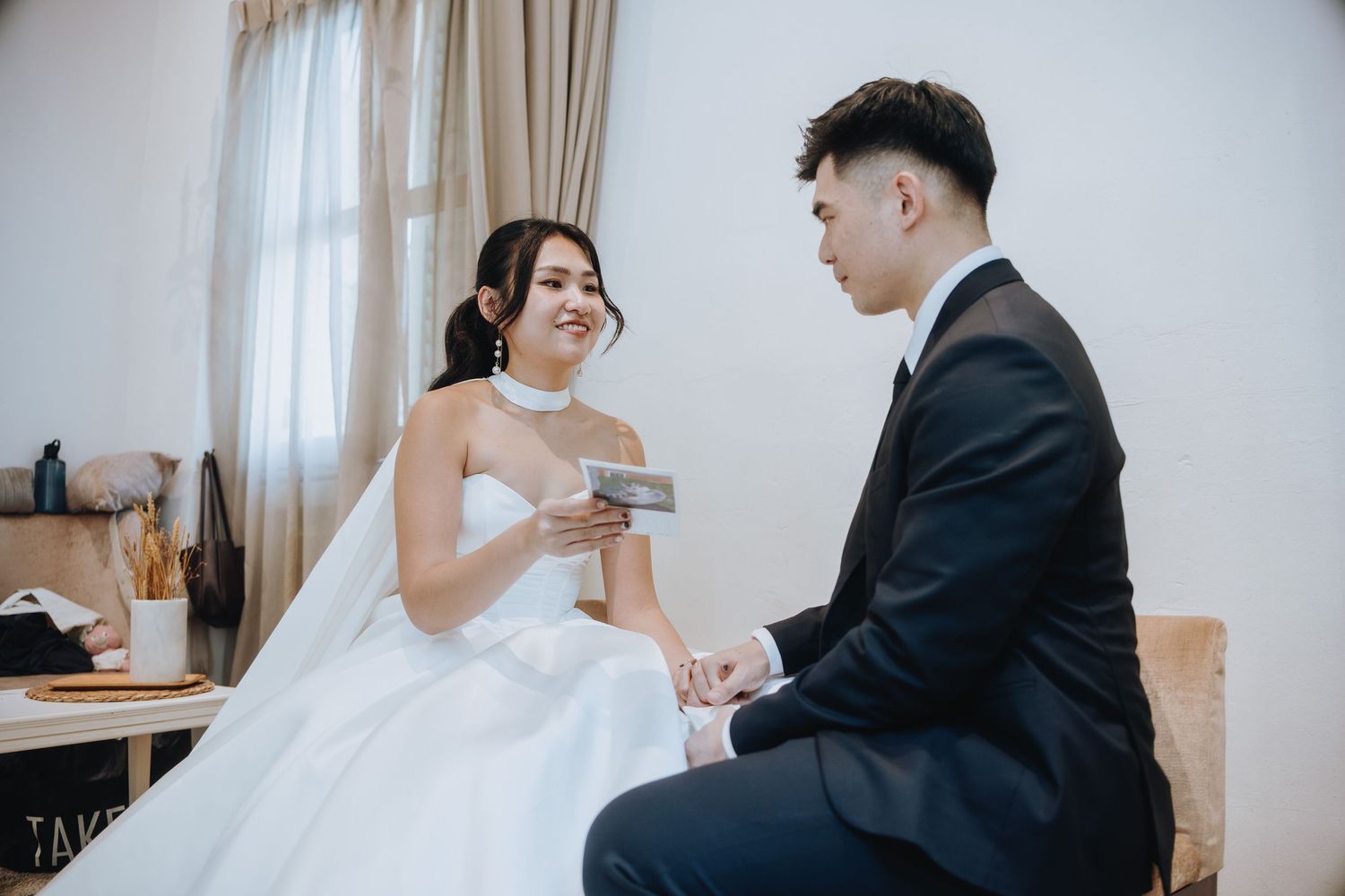 Bride in strapless gown and groom in suit sharing an intimate moment indoors.