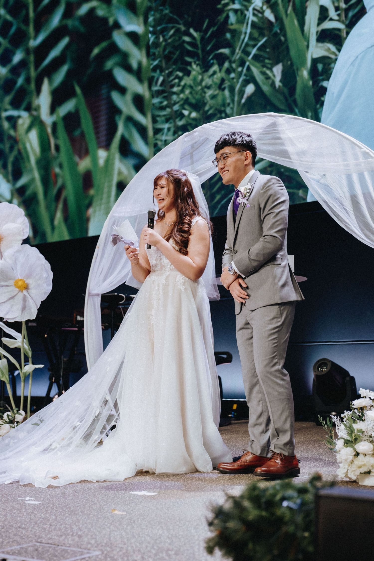 A bride and groom share a romantic kiss during their outdoor garden wedding ceremony with flowing white decor.
