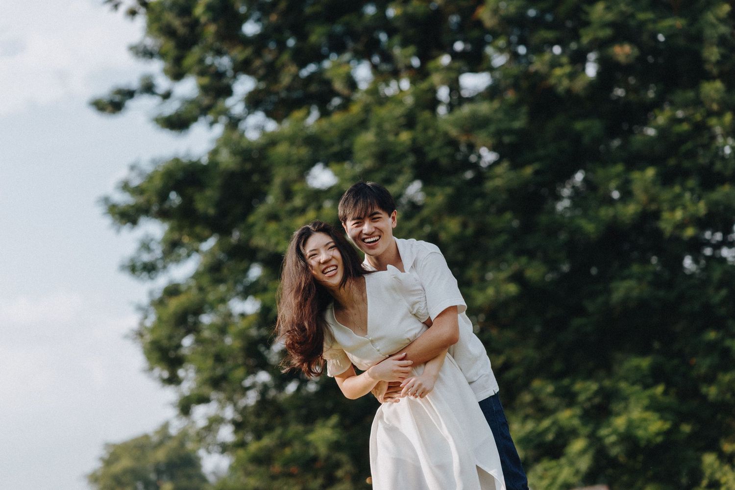 Couple sharing a joyful embrace outdoors with green trees in the background during a sunny afternoon.