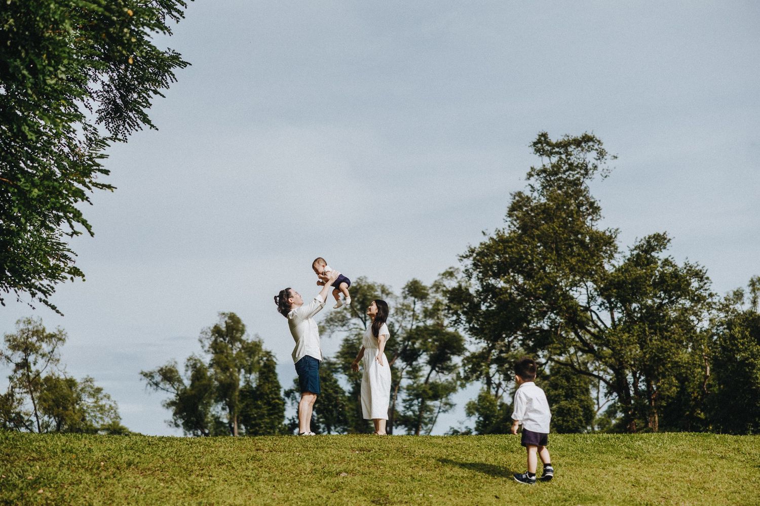 People playing and running together on a green grassy hill on a cloudy summer day.