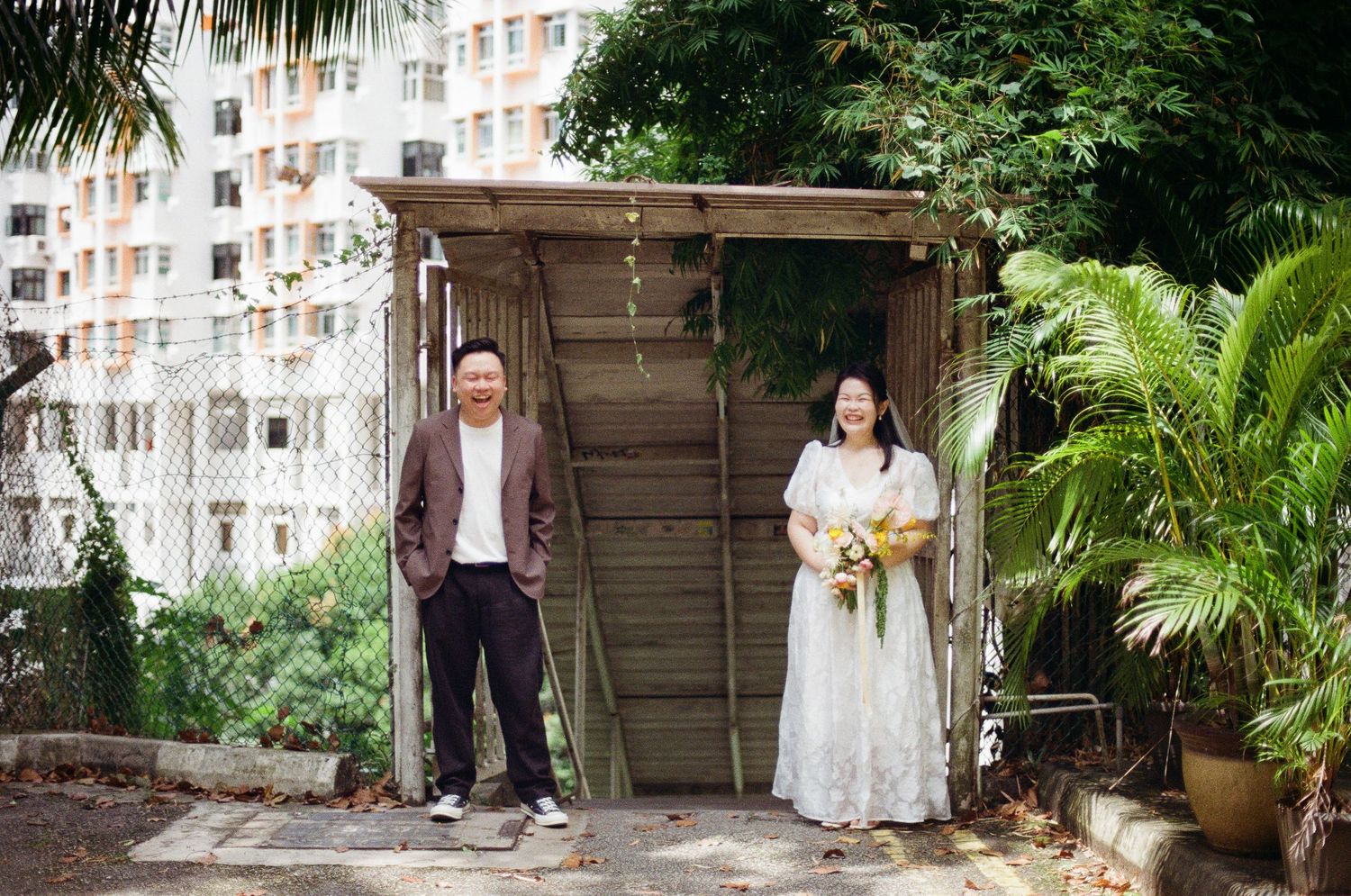 Wedding couple explores lush tropical garden pathway with palm trees and greenery surrounding their outdoor ceremony venue.