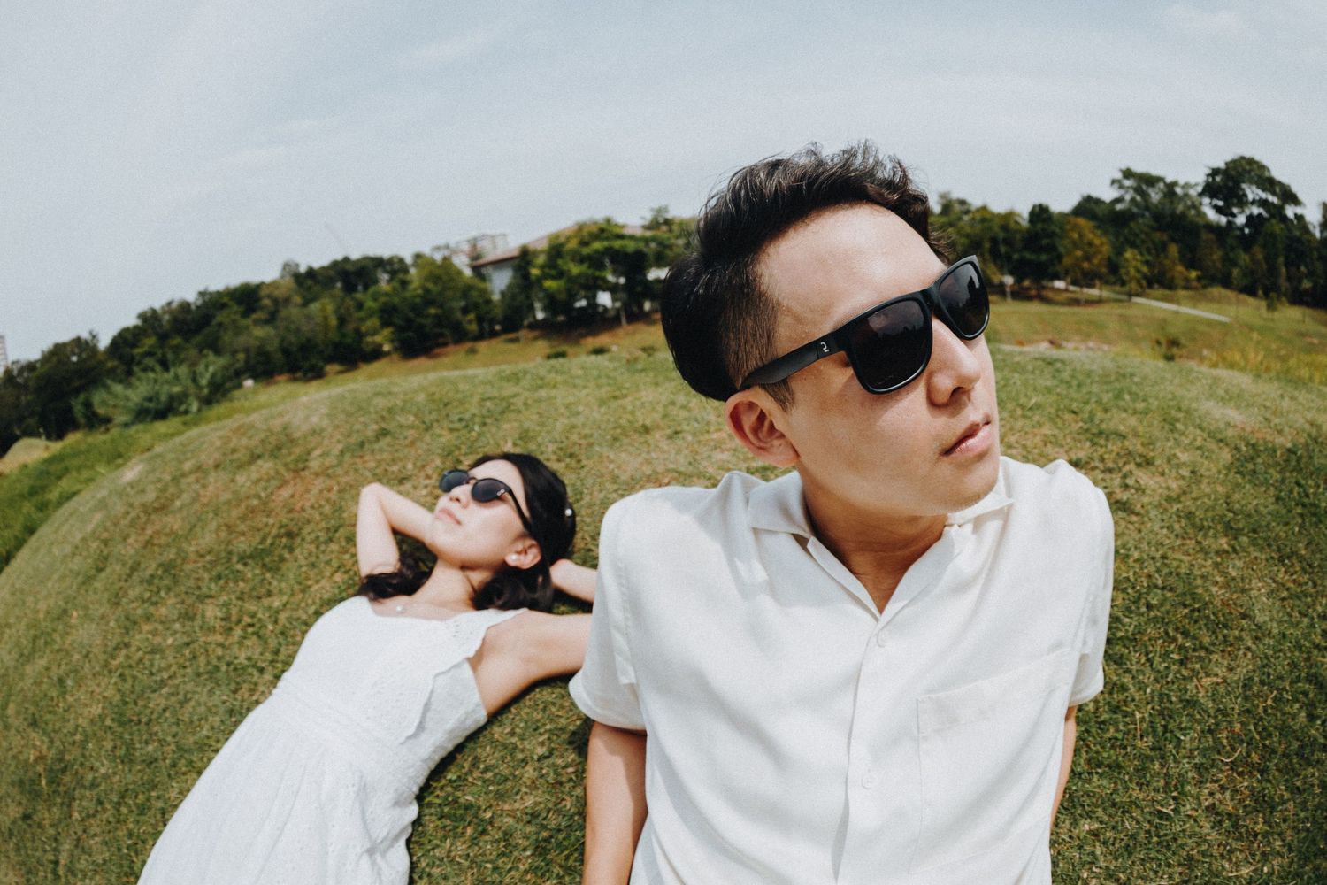 Artistic couple poses on grassy hillside with fisheye lens effect creating unique perspective.