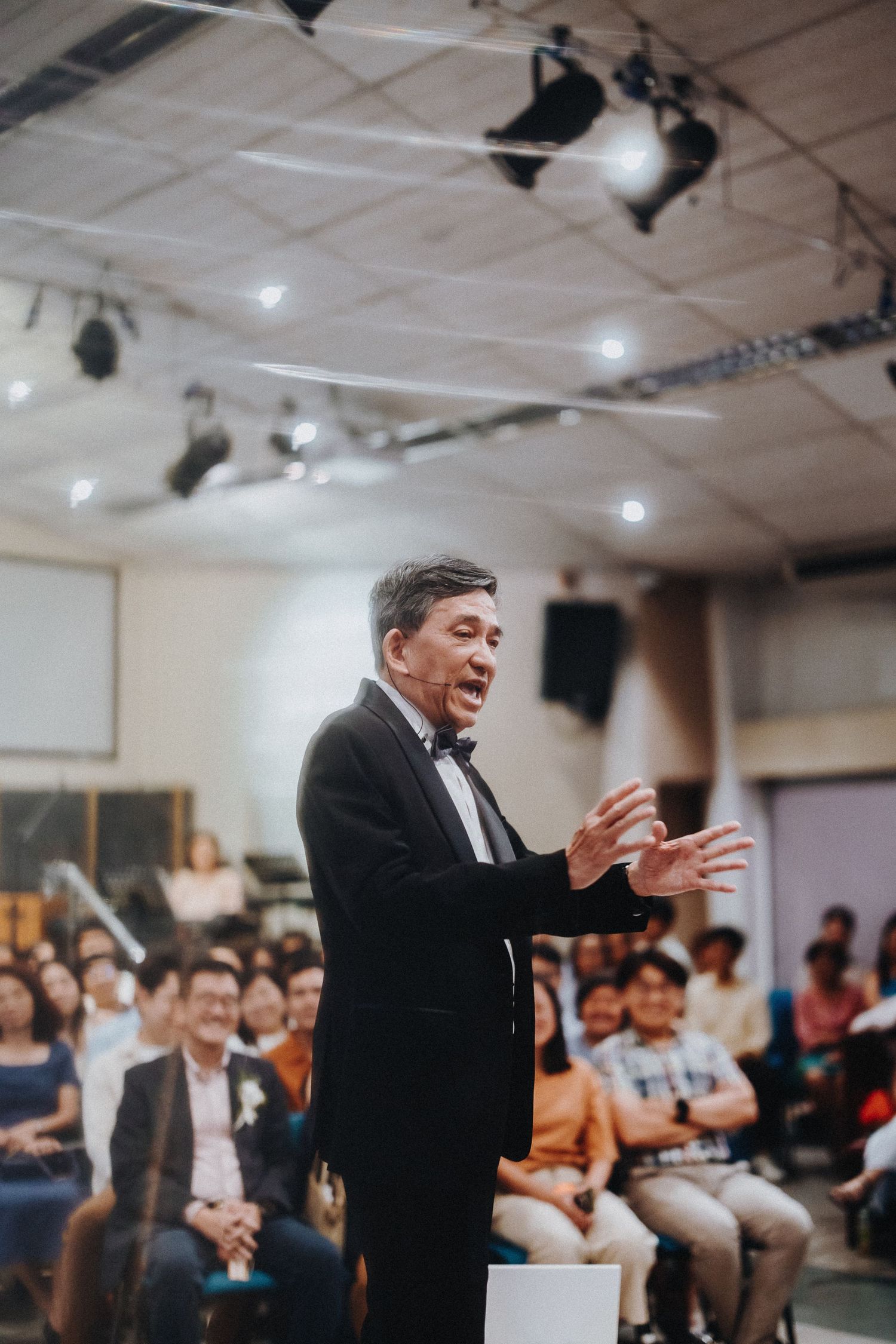 Speaker in formal attire gesturing passionately during presentation to audience.