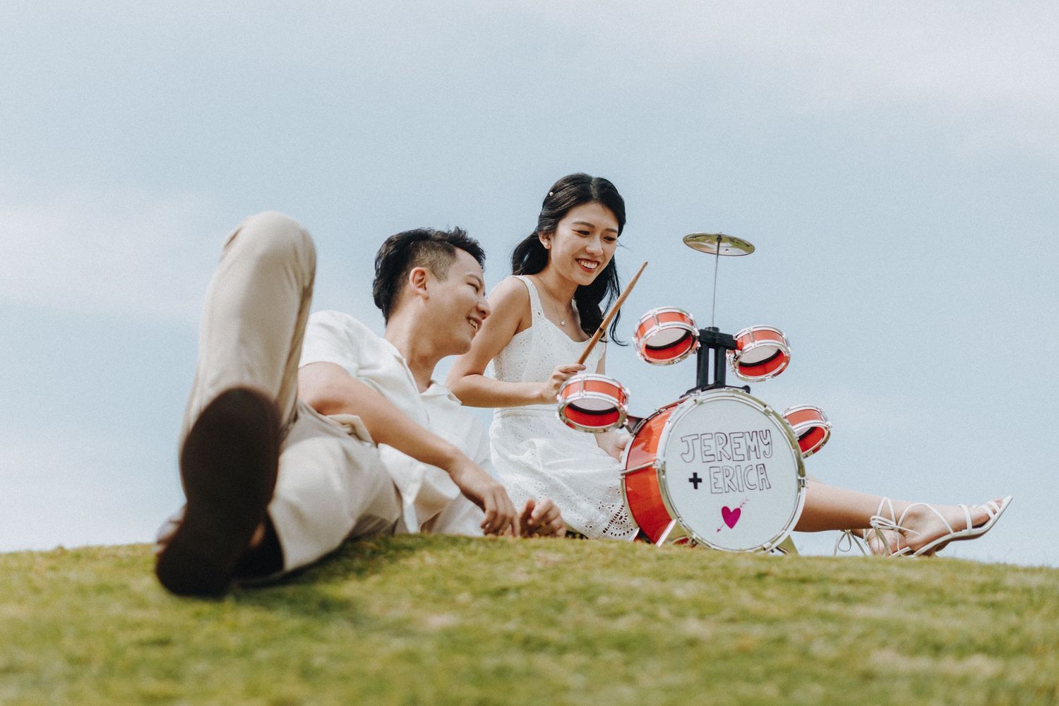 Couple relaxing on a grassy hillside with a picnic setup on a sunny day.