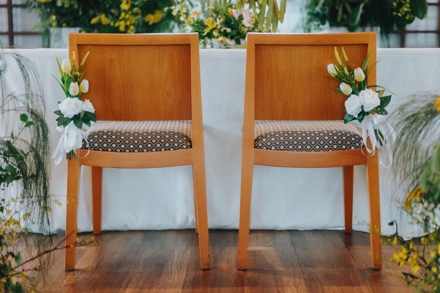 Two wooden chairs with patterned cushions decorated with white floral arrangements on an indoor deck.