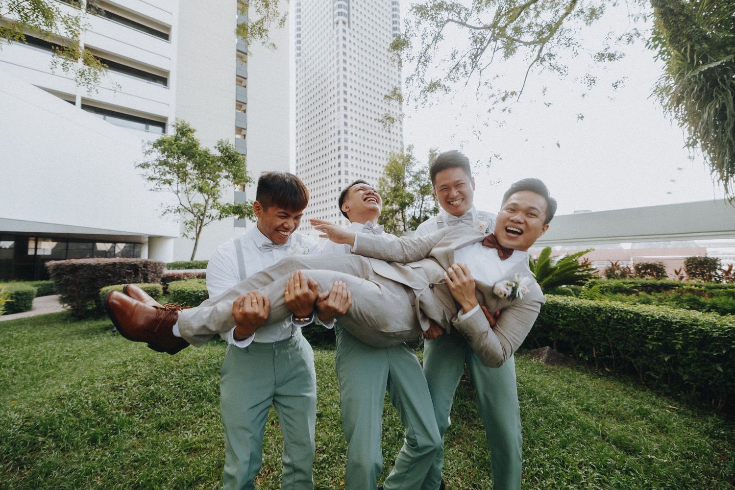 Fun candid moment of groomsmen carrying someone outdoors in matching mint green pants.
